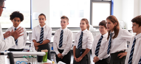 Schoolchildren lined up listening to a teacher.