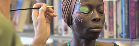 Woman getting her face painted with green swirls.
