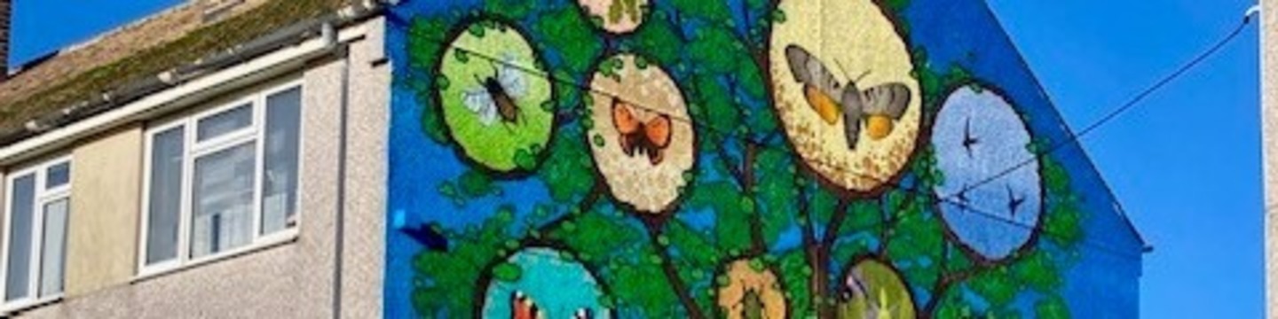 Colourful mural of a tree with wildlife illustrated in its leaves, painted on the side of a house.