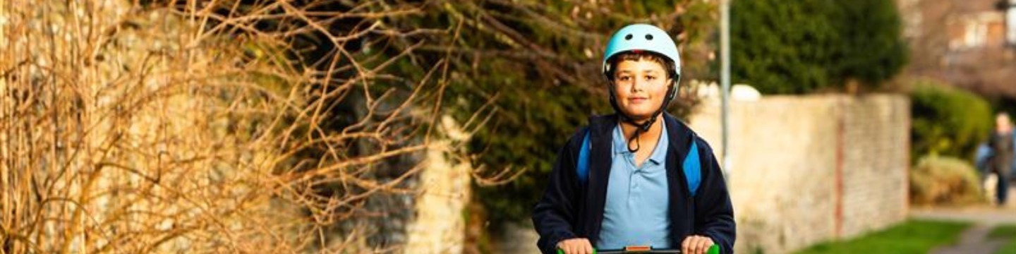 Young person using a scooter and wearing a helmet.