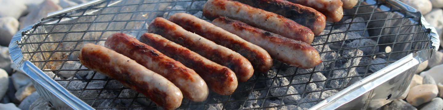 Sausages cooking on a disposable barbeque on a shingle beach.