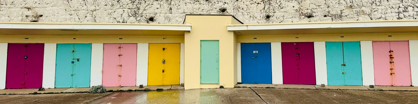 Beach huts in Saltdean with bright coloured doors. Chalk cliffs can be seen in the background.