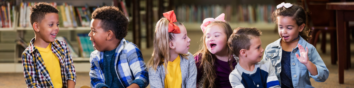 Group of young children smiling and chatting to one another in a library setting.
